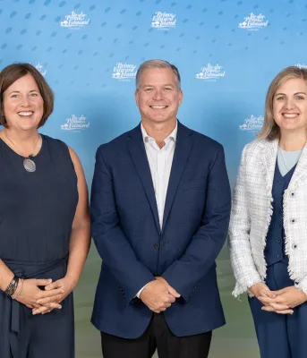 mage of three people in a room, standing shoulder to shoulder between to Prince Edward Island flags