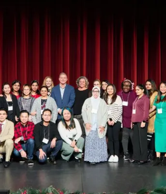 image of a group of people standing shoulder to shoulder on a stage with curtains in the background