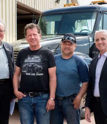 Six people standing with a large truck in the background.