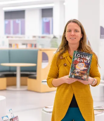 image of a person standing in a library holding a book in front of her