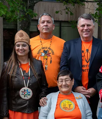 image of a group of people some in colourful ceremonial clothing standing shoulder to shoulder in front of a building