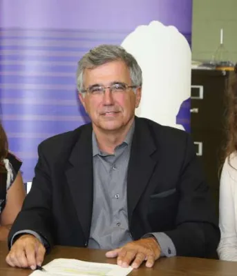 Two women sitting at a table with Minister Richard Brown with purple banner stand in background