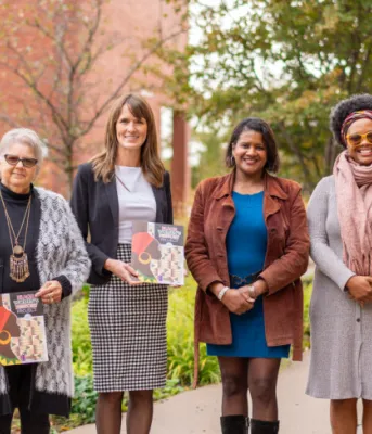 image of six people standing shoulder to shoulder if font of a brick building