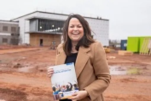 image of a person holding a document while standing in front of a building under contruction