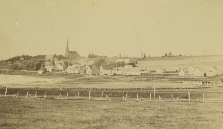 Community of St. Peters, Prince Edward Island, ca. 1870-1880. A wooden bridge across the St. Peters Bay can be seen, as well as a church in the background. Several other buildings and structures are also visible. A small boat is in the lower left corner.