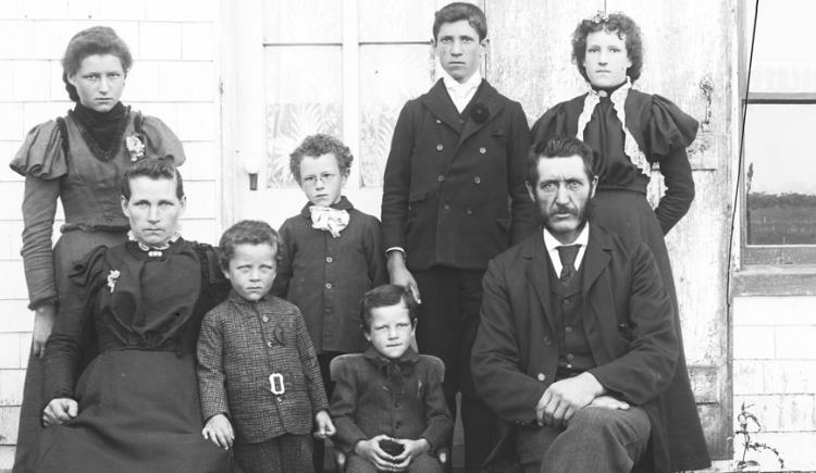 Family consisting of a man, woman, and six children posing for photograph in front of a house