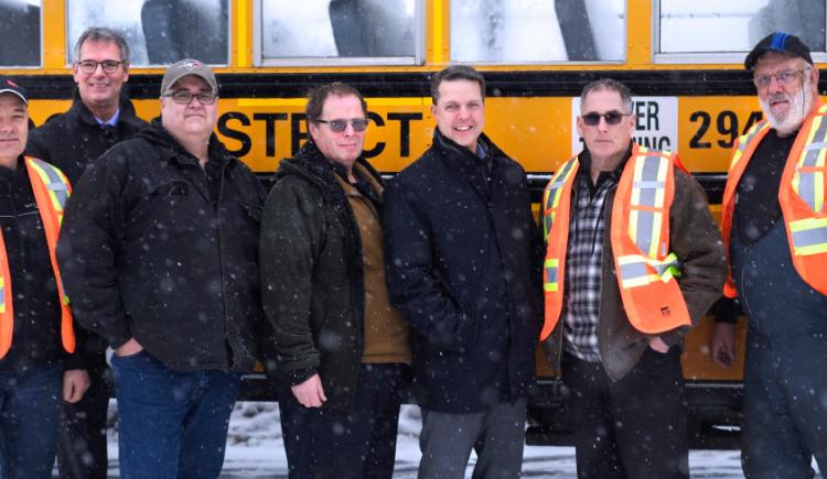 Minister Trivers and PSB Director Parker Grimmer stand outside beside a bus with school bus driver training participants