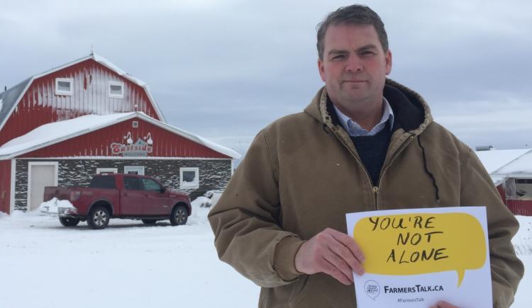 Image of Minister Bloyce Thompson in front of his barn holding a Farmers Talk sign that reads "You are not alone"